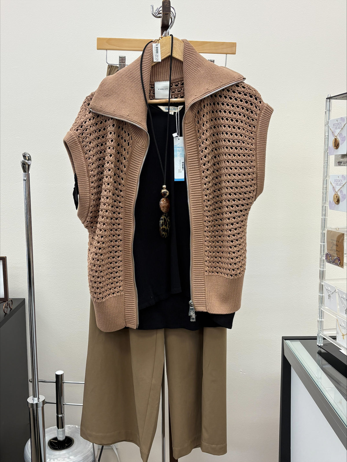Brown knitted vest and pants on a hanger against a white wall.