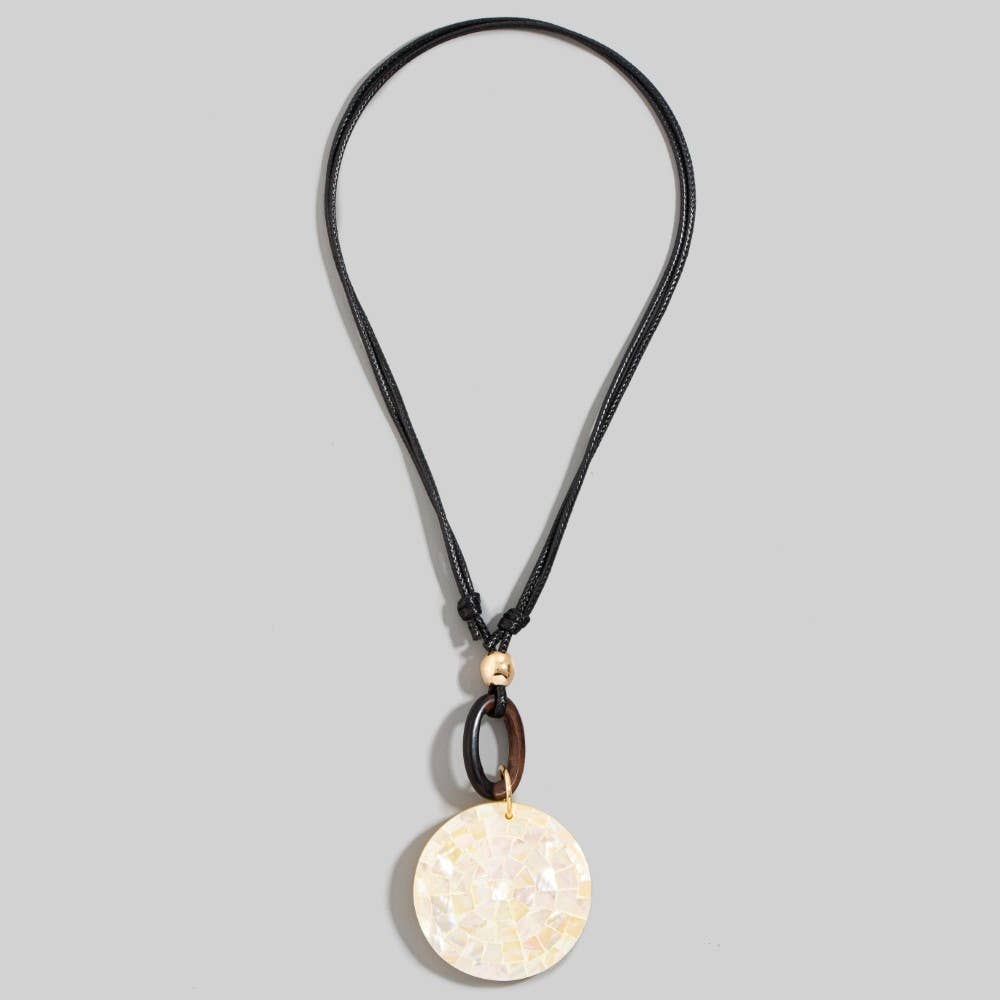 A black cord necklace featuring a circular pendant made of iridescent mother-of-pearl tiles, accented by a dark brown wooden ring and a small gold bead, shown against a solid gray background.