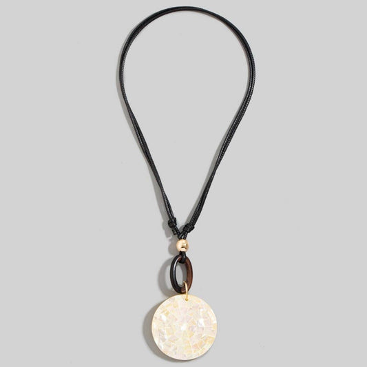 A black cord necklace featuring a circular pendant made of iridescent mother-of-pearl tiles, accented by a dark brown wooden ring and a small gold bead, shown against a solid gray background.