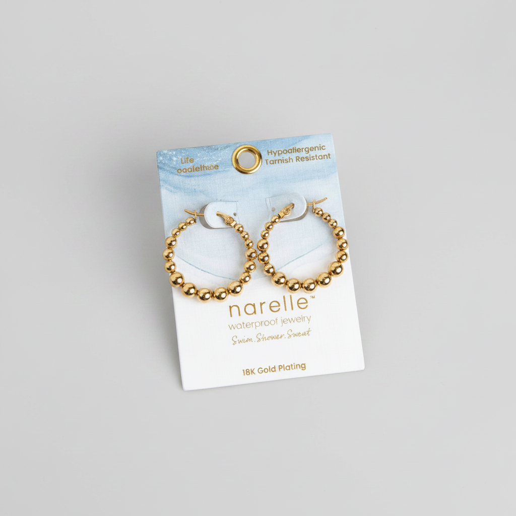 Gold hoop earrings on a Narelle jewelry card with flowers in the background