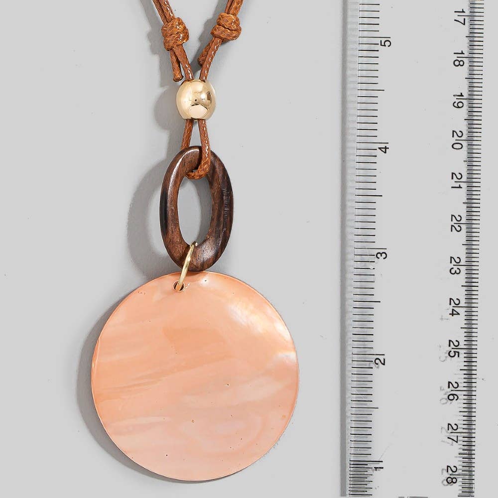 Necklace with a large round peach-colored pendant and brown cord, next to a ruler for scale.
