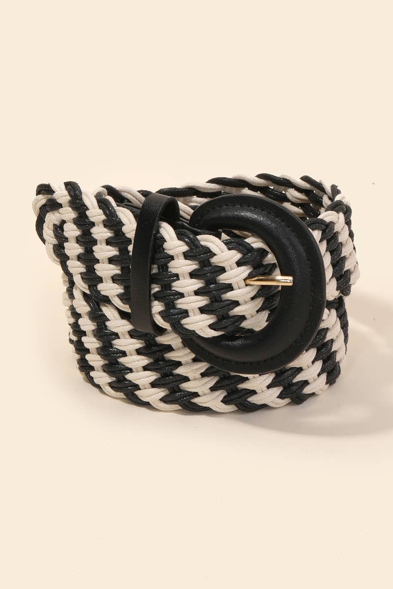 A thick braided rope belt in black and off-white, featuring a large black faux-leather circular buckle with a small gold metal tip, set against a solid cream background.