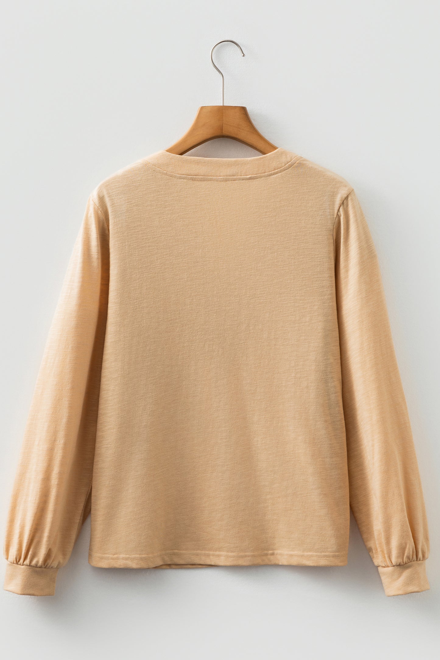 Beige long sleeve V-neck top by Chic Speak Boutique, displayed on a hanger with a smooth fabric texture and casual fit.