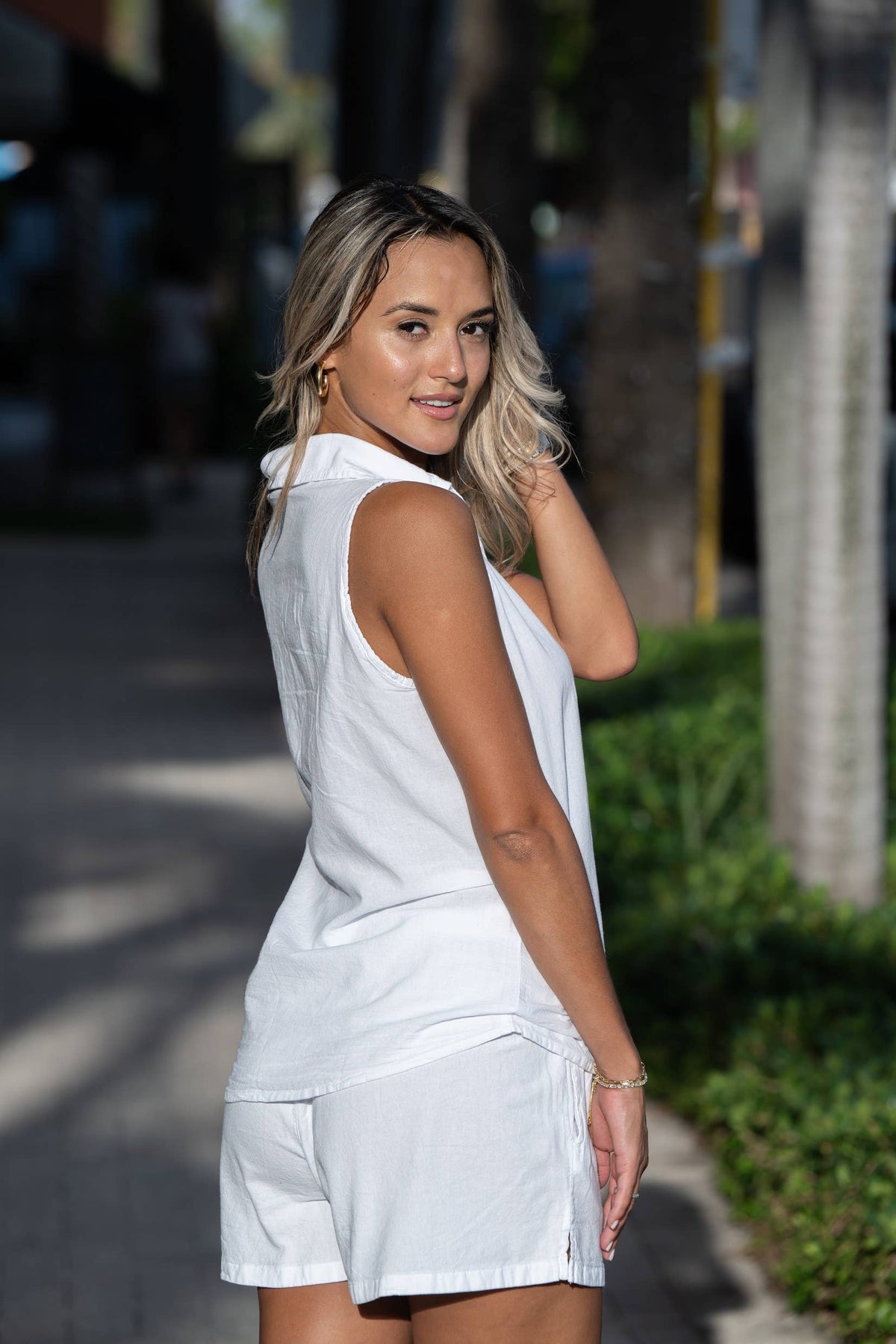 Astra women's sleeveless high-low cotton top with button-up front, natural white fabric, and casual stylish design.