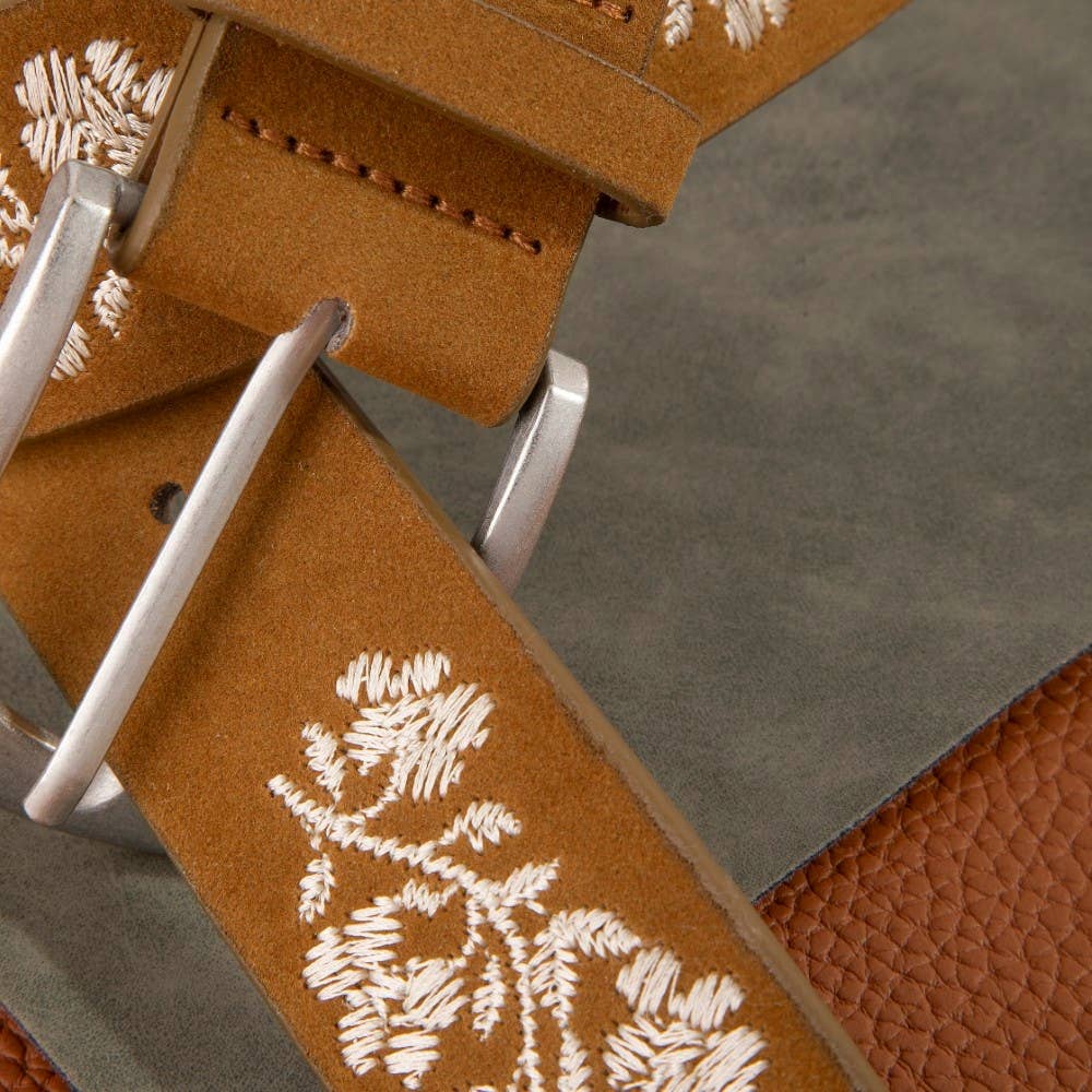 Close-up of a brown leather belt with floral embroidery and silver buckle on a textured surface.