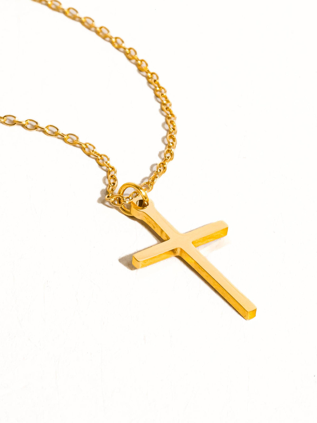 Flanerie by MAIQ Tirza 18K gold non-tarnish small cross necklace hanging on a chain against a white background.