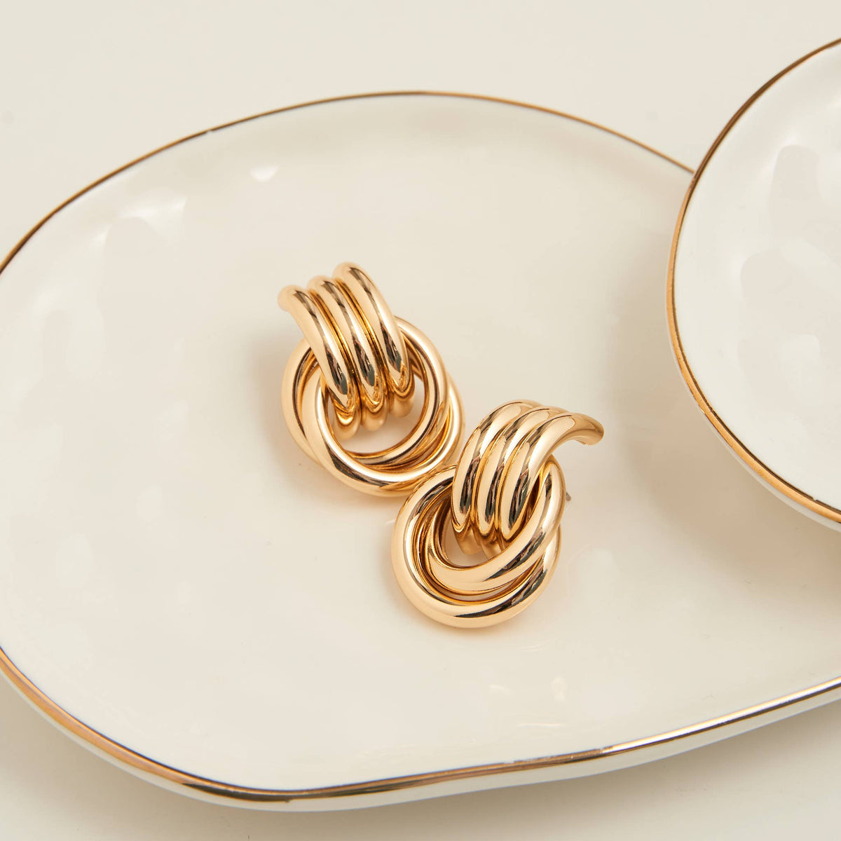 Howard's Stud Earrings Solara Interlocking Triple Knot, gold-tone jewelry with intertwined knot design, close-up view of earrings.
