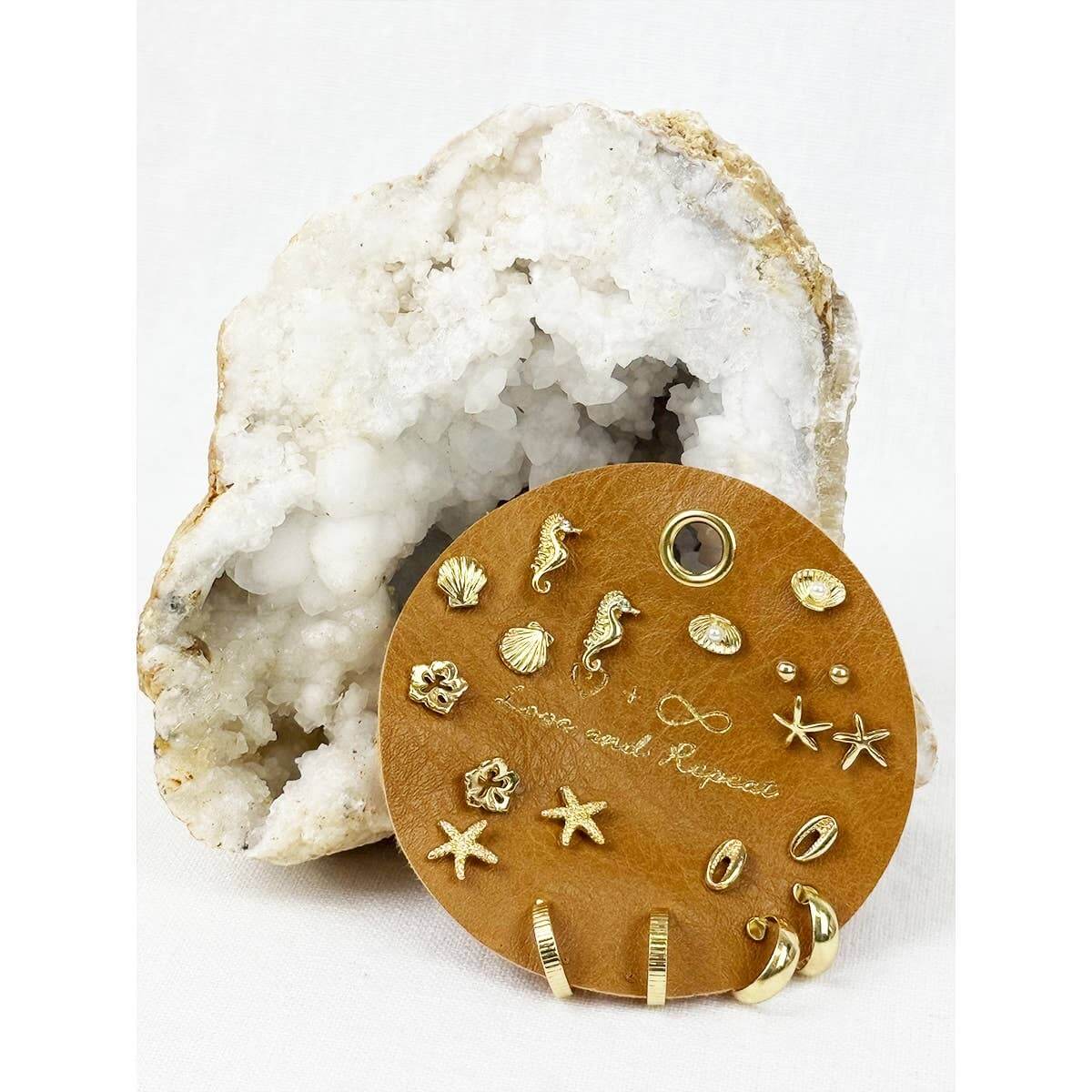 Beach-themed earrings by Love and Repeat featuring seashell and starfish designs on silver hooks.