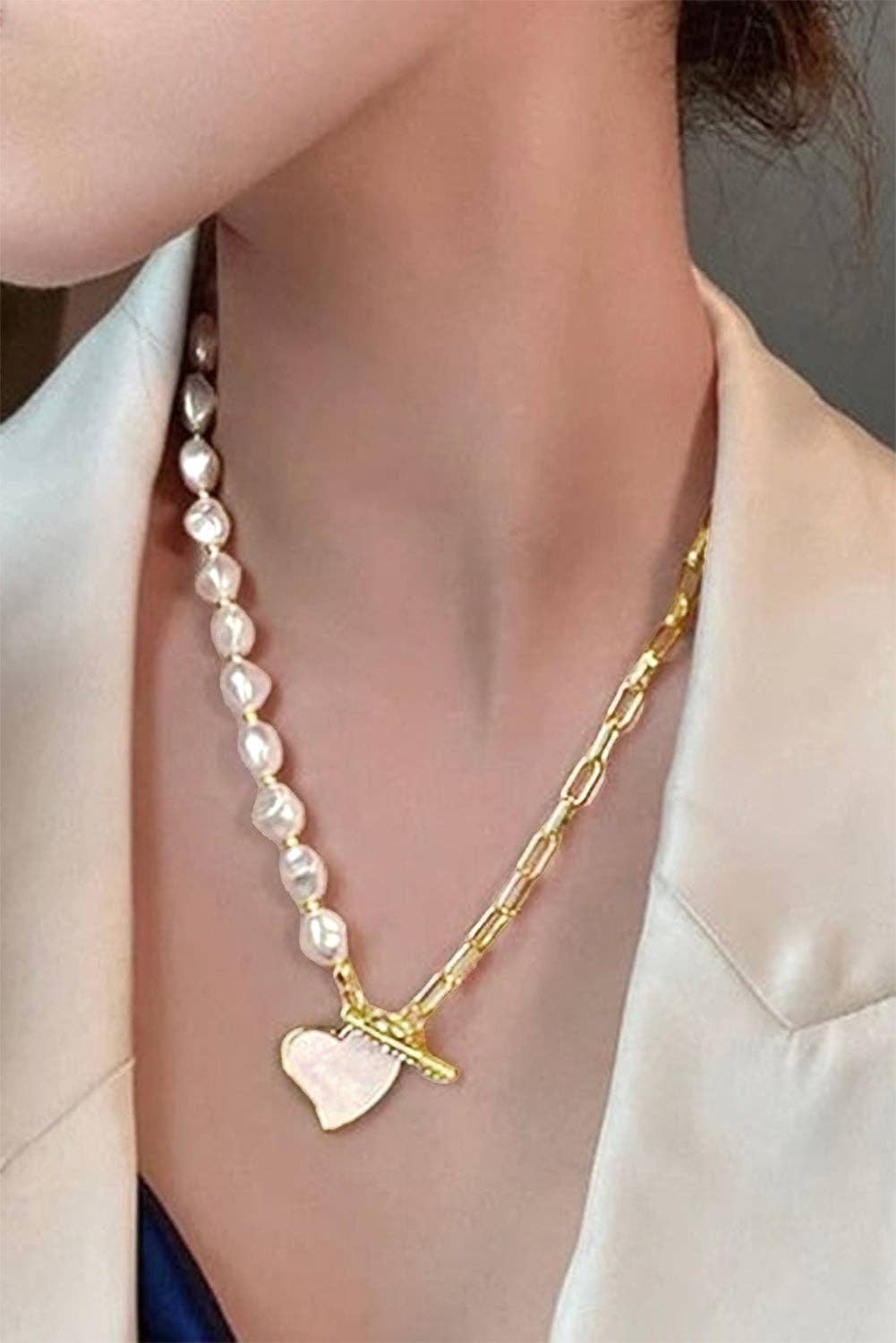 Gold heart-shaped pendant necklace with rhinestone accents and pearl chain from Lovesoft, close-up view of the jewelry.