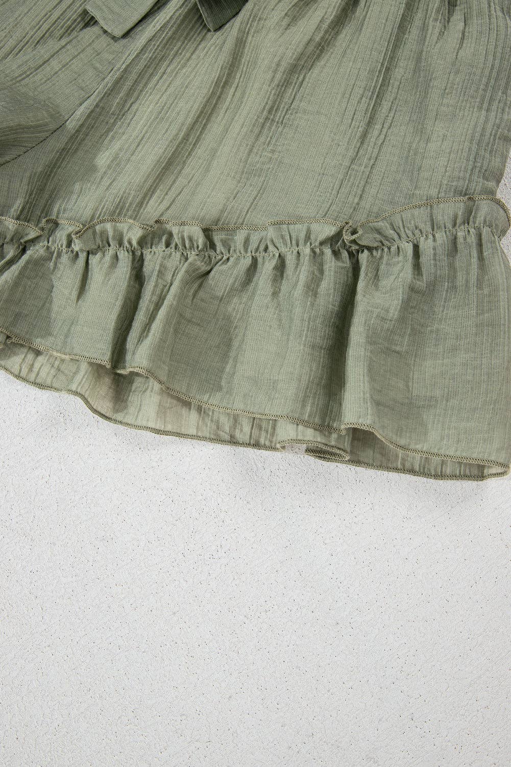 Laurel green textured tie waist shorts with ruffle hem, by Lovesoft, shown in a close-up image highlighting fabric and design details.