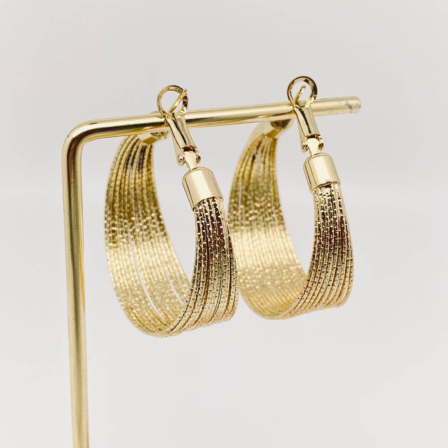 Golden multi-layer coil hoop earring by Mio Queena featuring layered coil design and shiny finish.