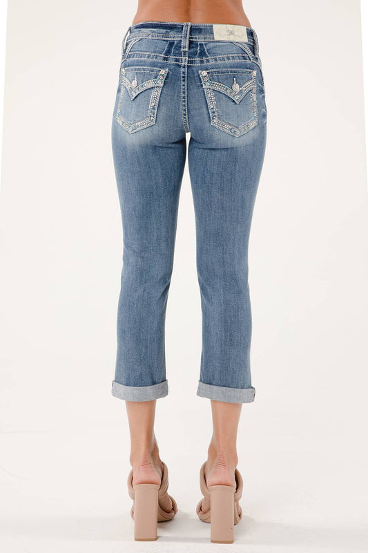 Miss Me mid-rise Capri jeans in classic denim with distressed details and rolled cuffs, displayed on a neutral background.