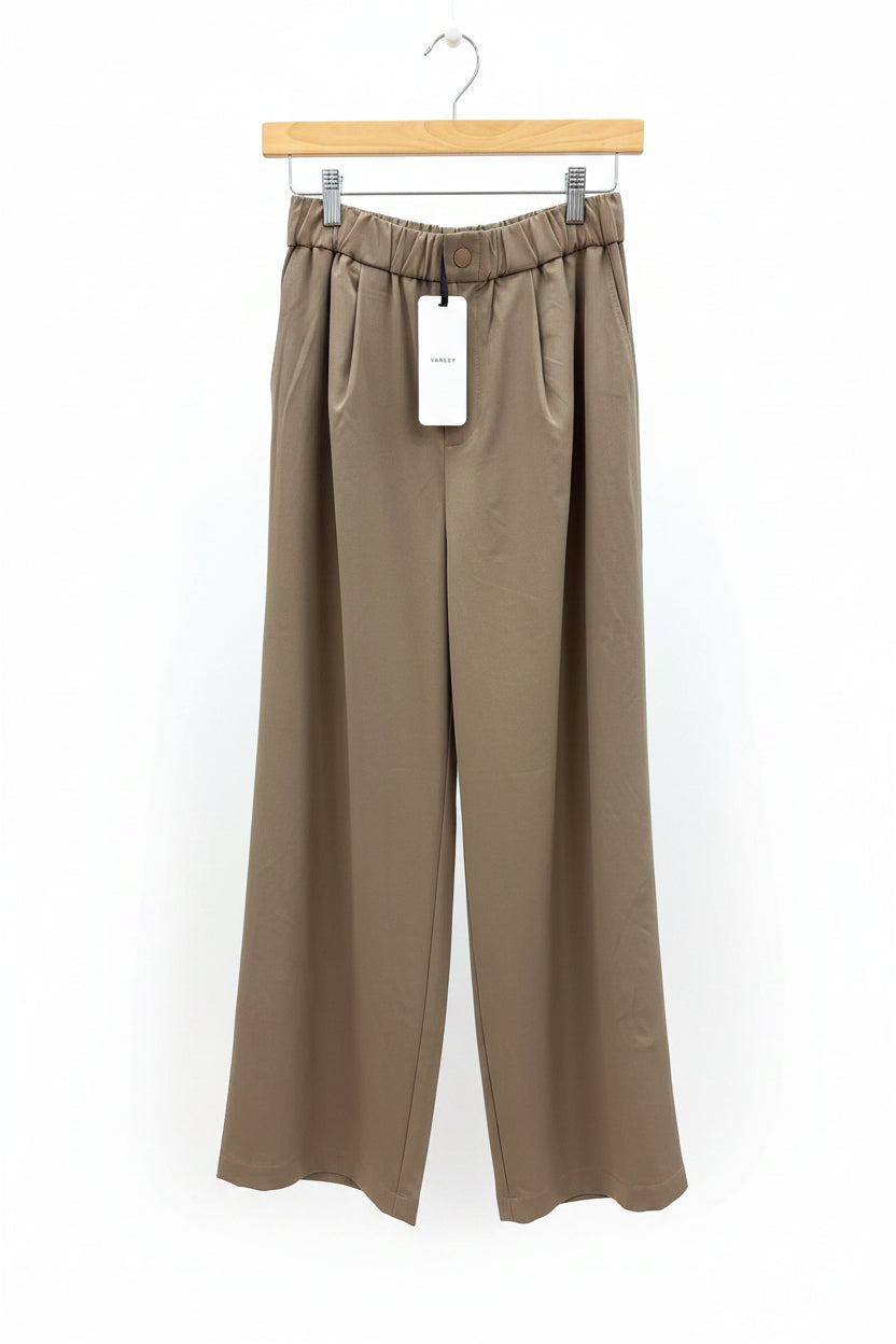 Brown pants on a hanger with a tag against a wooden panel background