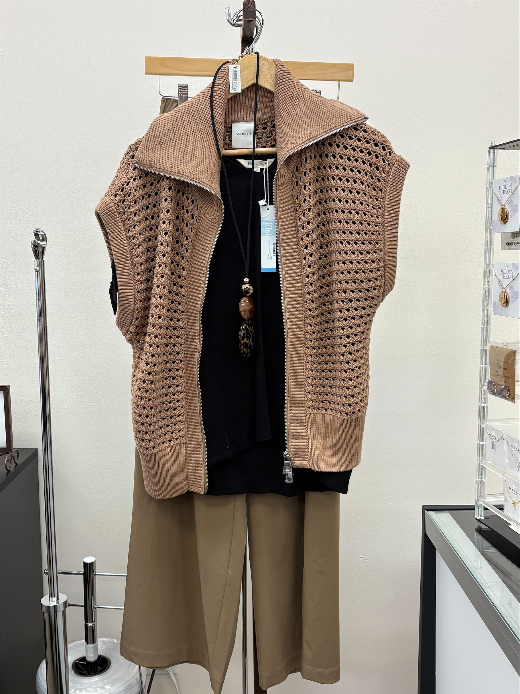 Brown knitted vest and pants on a hanger against a white wall.