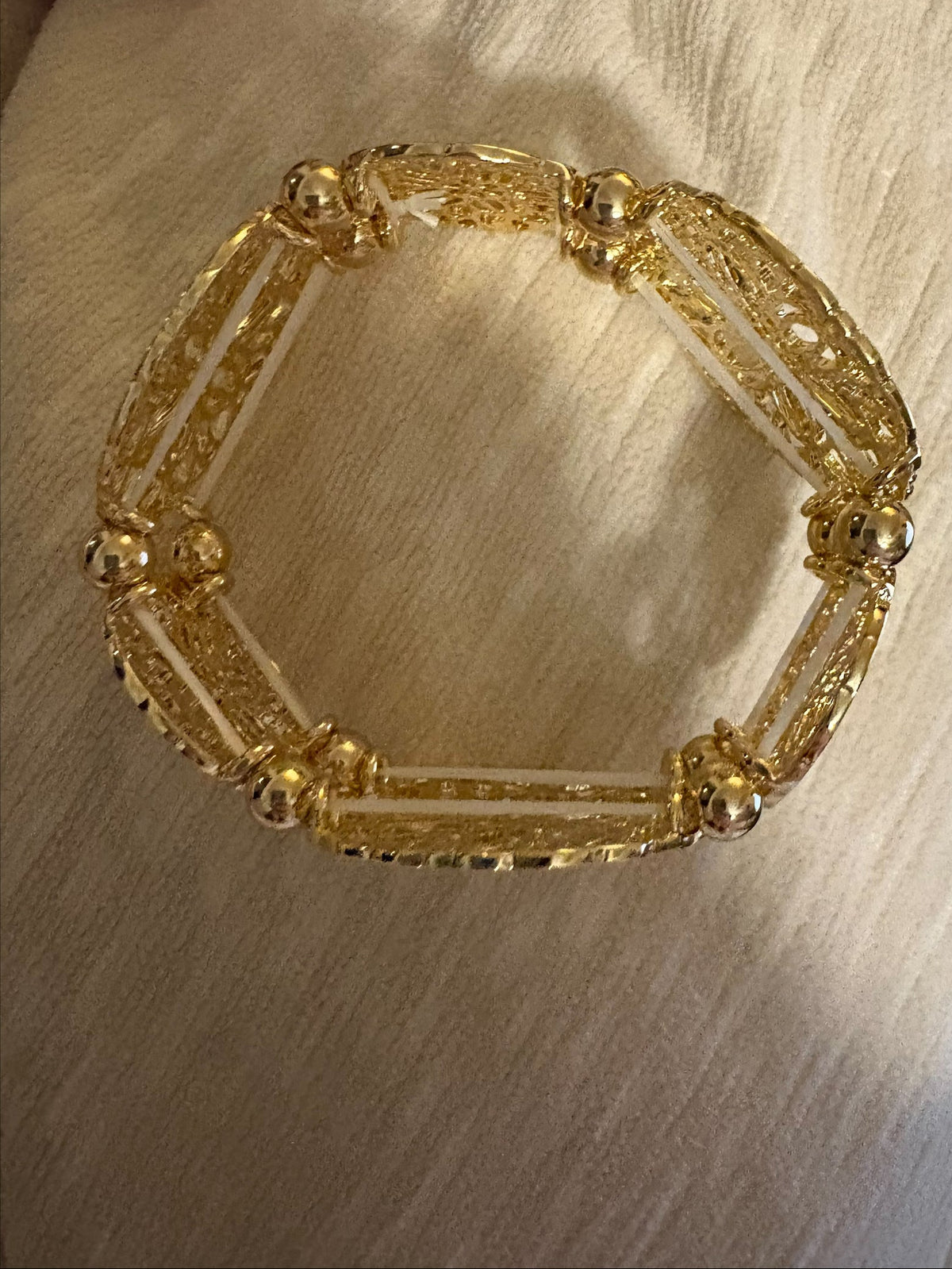 Gold filigree stretch bangle bracelet by S&A Fashions with intricate openwork design on smooth, flexible band.