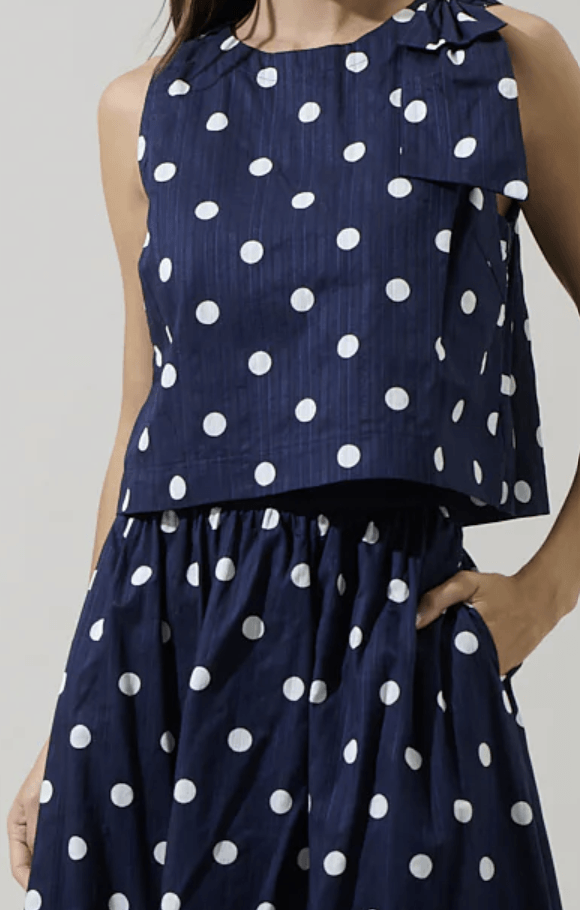 Sugarl!ps Caryn polka dot sleeveless top displayed on a hanger, featuring a stylish sleeveless design and classic polka dot pattern.