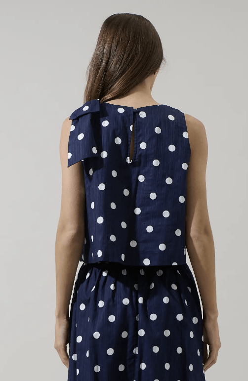 Sugarl!ps Caryn polka dot sleeveless top with ruffled neckline and bow detail, featuring a playful black and white pattern.